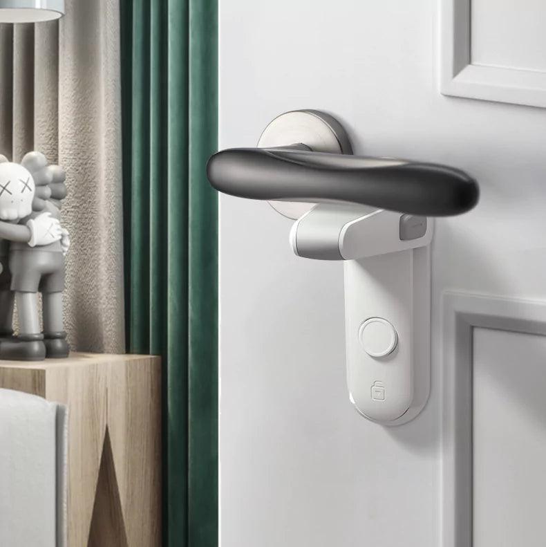 Ett vitt barnlås är monterat under ett svart dörrhandtag på en vit dörr. Låset är aktiverat och hindrar handtaget från att tryckas ned. I bakgrunden syns ett rum med gardin och en hylla med dekorationer.