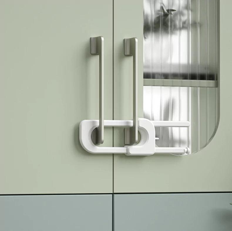 Vitt barnlås för dubbeldörr med handtag, monterat för att hindra barn från att öppna skåpsdörrar.