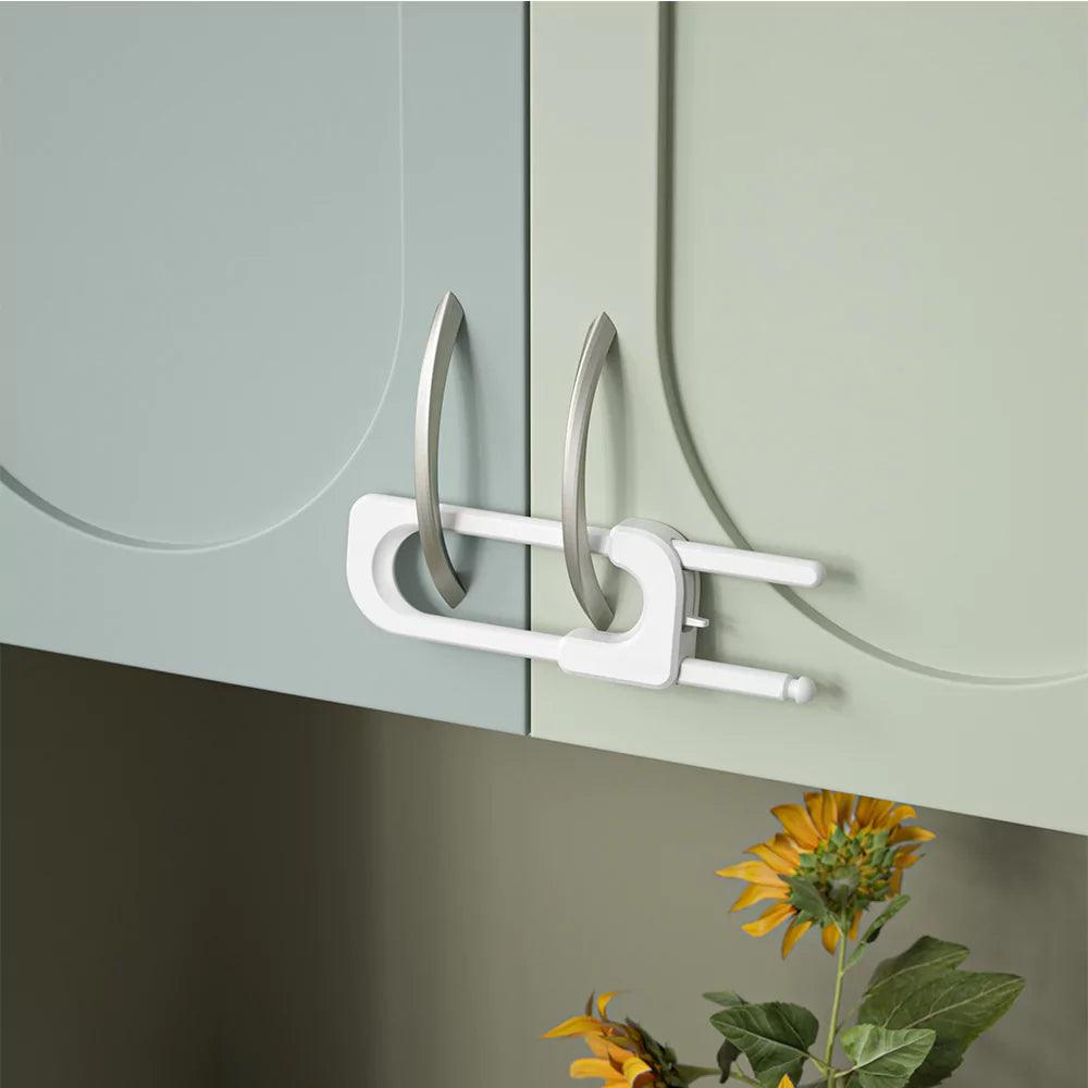 Vitt barnlås för dubbeldörr med handtag monterat på köksskåp för att förhindra att barn öppnar dörrarna.