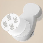 Närbild av ett vitt automatiskt klämskydd för dörrar, visat med en rund självhäftande 3M-tejp på baksidan för montering.