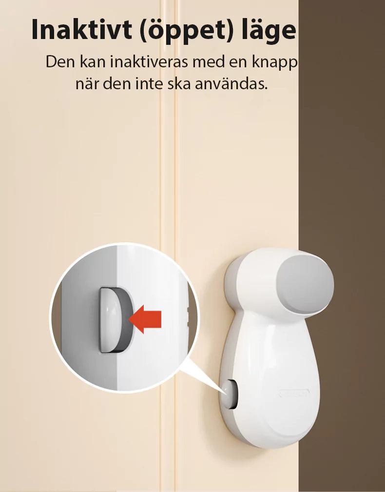 Bild som visar ett vitt automatiskt dörrklämskydd monterat på en dörrkarm. En inzoomad cirkel markerar en knapp med en röd pil som pekar på den, vilket visar hur skyddet kan sättas i inaktivt (öppet) läge när det inte ska användas.