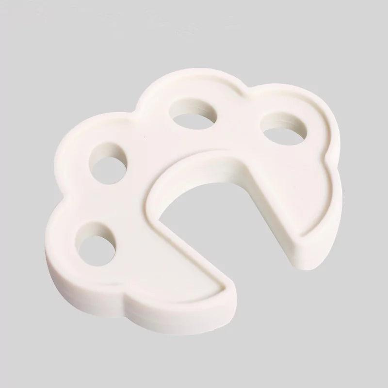 Vitt skumklämskydd i form av en blom- eller tassliknande figur med ett U-format spår som placeras på dörrkanten för att förhindra att dörren stängs helt.