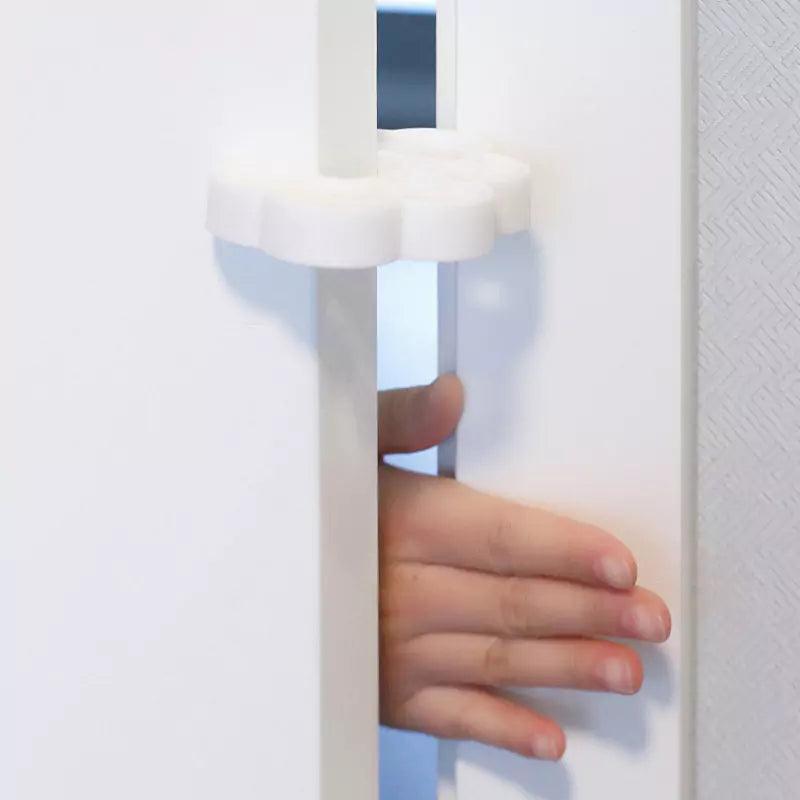 Ett vitt skumklämskydd sitter på dörrkanten och håller dörren öppen så att en barns hand inte riskerar att klämmas.