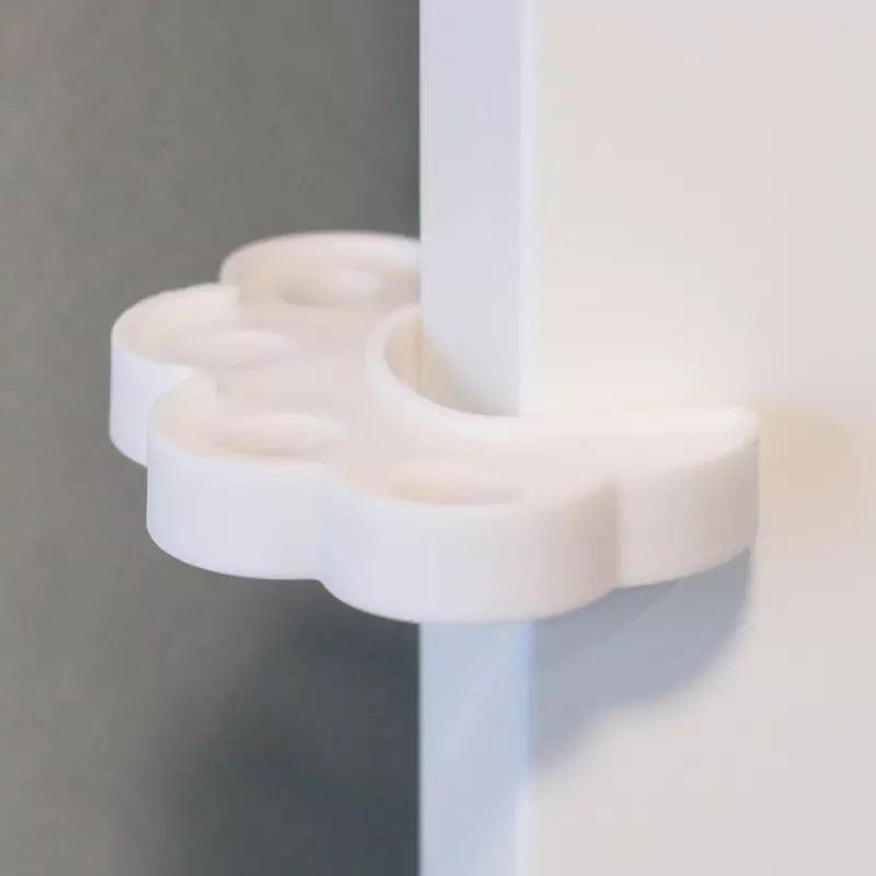 Ett vitt skumklämskydd i form av en blomliknande kudde sitter monterat på dörrkanten för att hålla dörren lite öppen och förhindra att fingrar kläms.