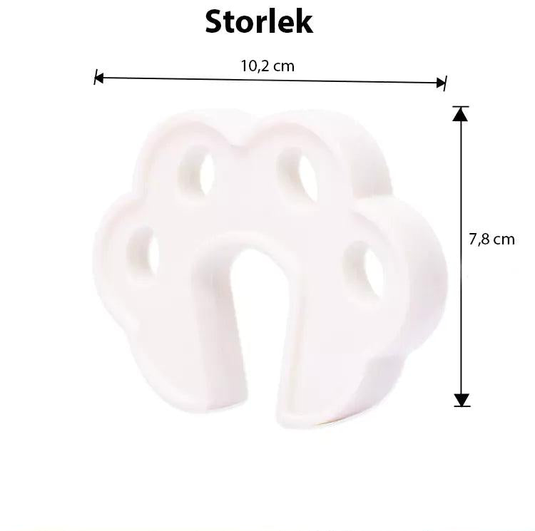 Vitt blomformat dörrklämskydd i skum med måtten 10,2 × 7,8 cm, visat både ensamt och monterat på en dörrkant. Passar dörrar med tjocklek mellan 3,5 och 5 cm.