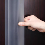 Hand som trycker på ett flexibelt, genomskinligt dörrklämskydd monterat på dörrens bakkant.