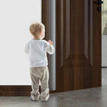 Litet barn som står vid en öppen dörr med ett monterat genomskinligt klämskydd på dörrens bakkant för att förhindra klämskador.