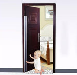 Litet barn som sitter på golvet vid en halvöppen dörr med ett monterat genomskinligt klämskydd längs dörrens bakkant för att förhindra klämskador.