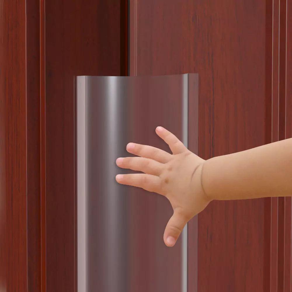 Ett barns hand sträcks mot ett genomskinligt klämskydd monterat på bakkanten av en trädörr.