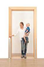 En vuxen person står i en dörröppning med ett litet barn på armen och räcker med den andra handen mot den infällda, hoprullade säkerhetsgrinden som sitter monterad på dörrkarmen.