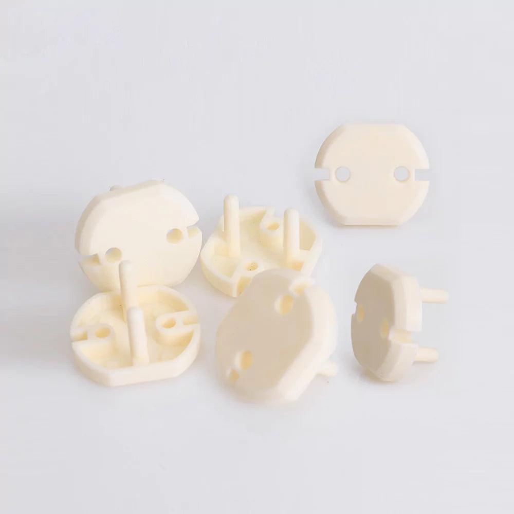 Vita petskydd för eluttag i EU-standard, visade både fram- och baksida. Flera skydd med två piggar ligger utspridda på en vit yta.