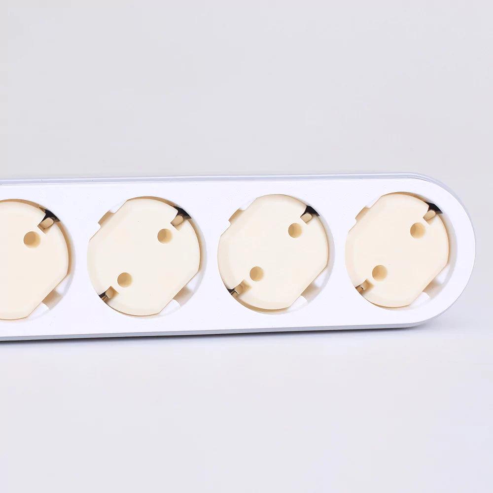 Flera vägguttag med monterade barnsäkra petskydd i ljus plast, placerade i en vit grenpropp av EU-typ.